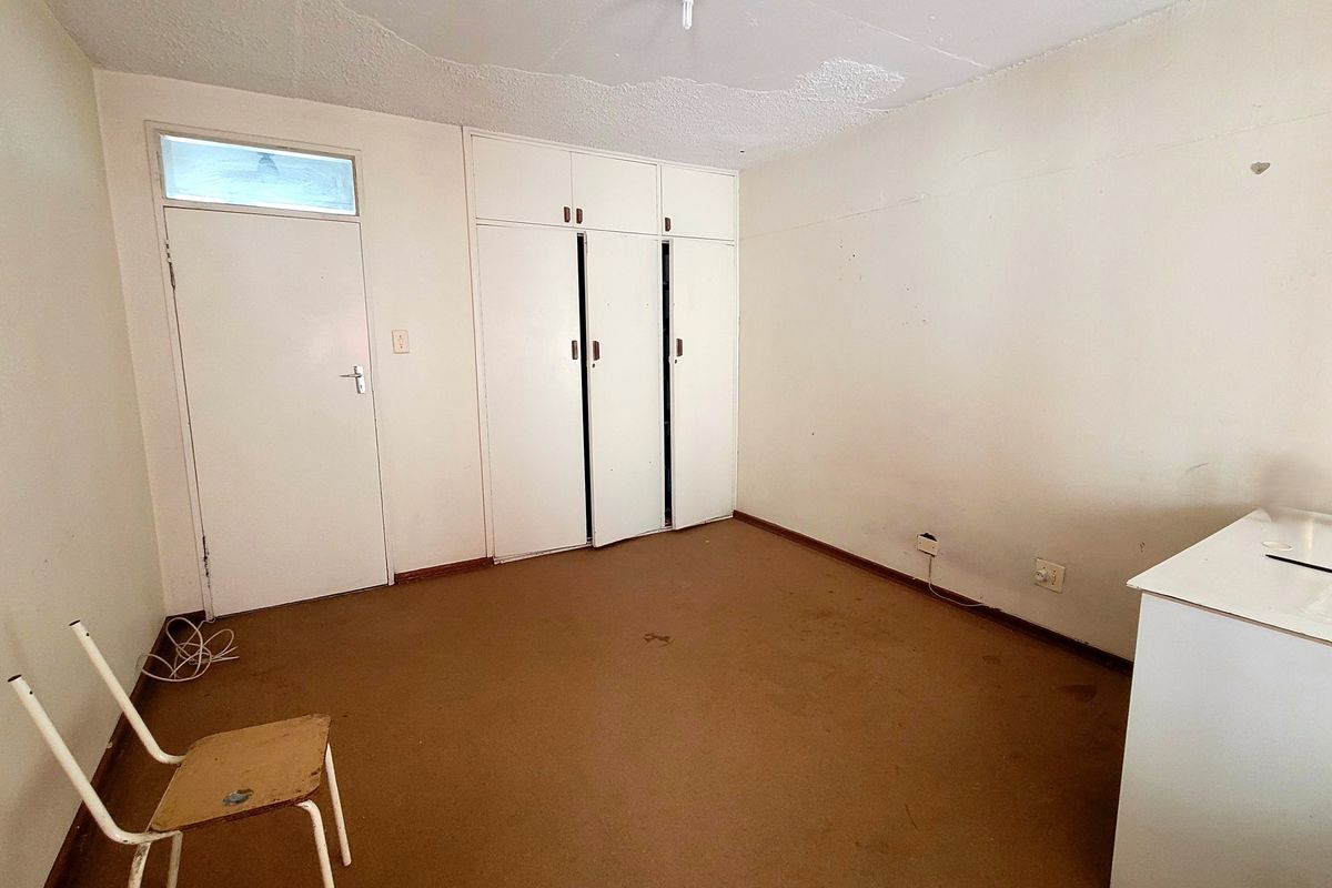 An empty bedroom featuring built-in cupboards, a transom window, and carpeted flooring, requiring cosmetic updates to improve its overall condition.