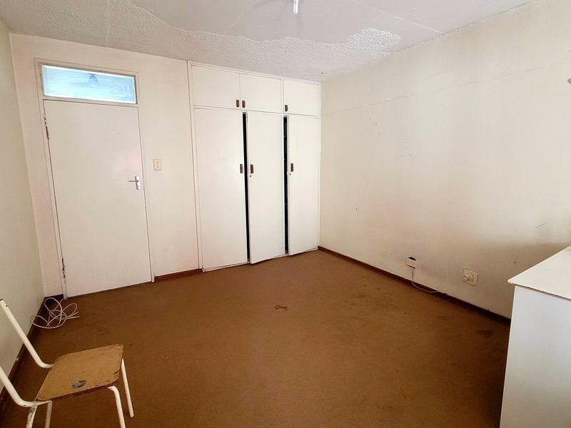 An empty bedroom featuring built-in cupboards, a transom window, and carpeted flooring, requiring cosmetic updates to improve its overall condition.