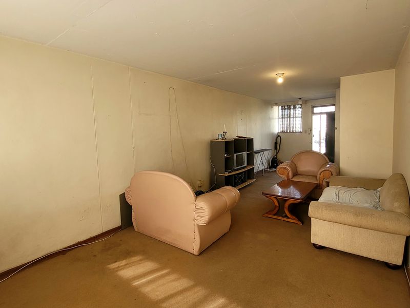 A living room area featuring carpet flooring and access to an exterior security gate, requiring cosmetic updates to wall finishes and flooring.