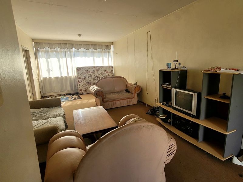 A living room area featuring carpet flooring and large windows with curtain tracks, requiring cosmetic updates and refurbishment to improve its overall condition.