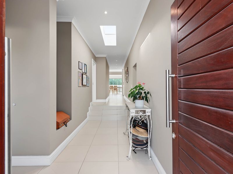 A bright and welcoming entrance hallway featuring tiled flooring, a skylight, and a solid timber front door leading into the home.