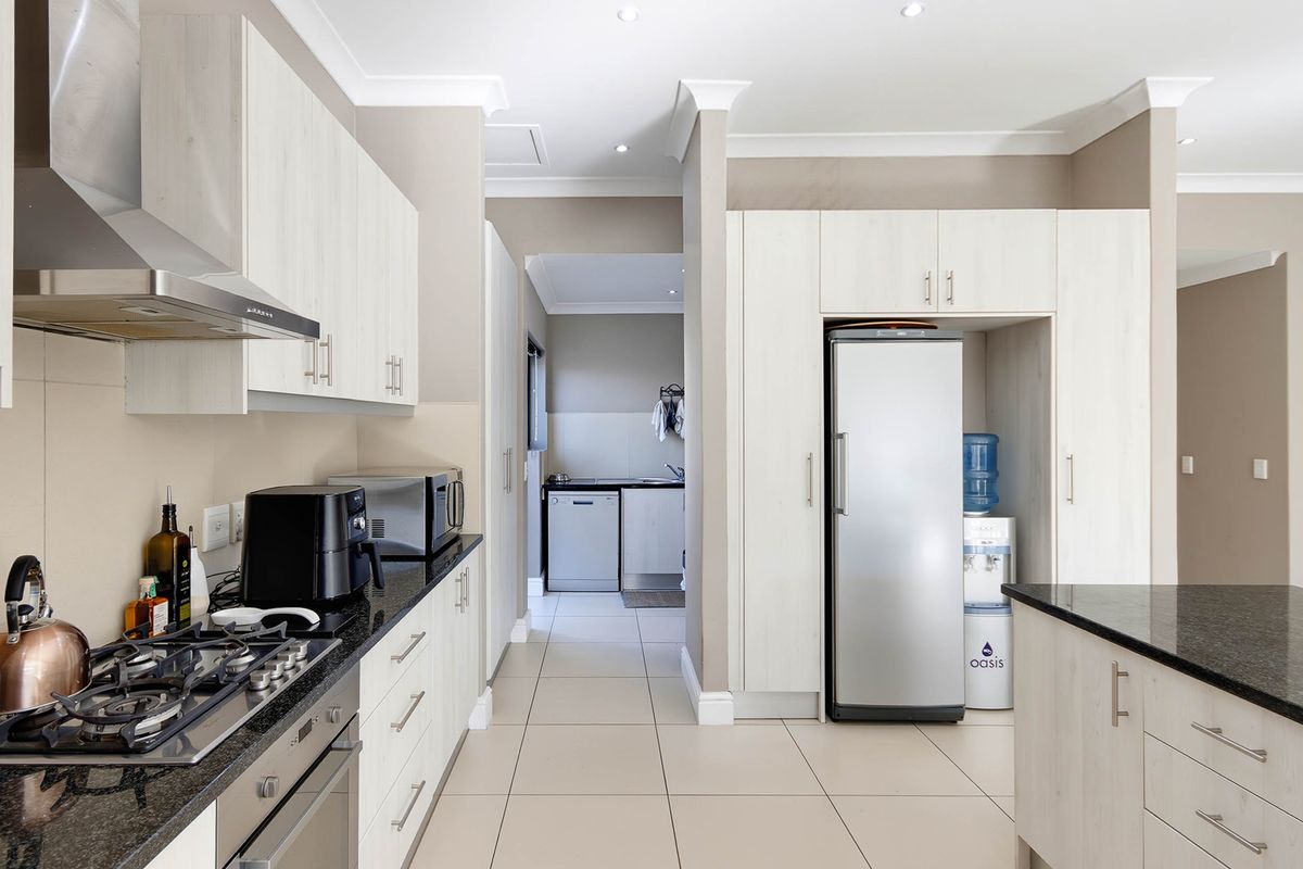 Modern kitchen featuring light wood cabinetry, granite countertops, gas hob, extractor fan, and integrated oven, with an adjacent scullery area.