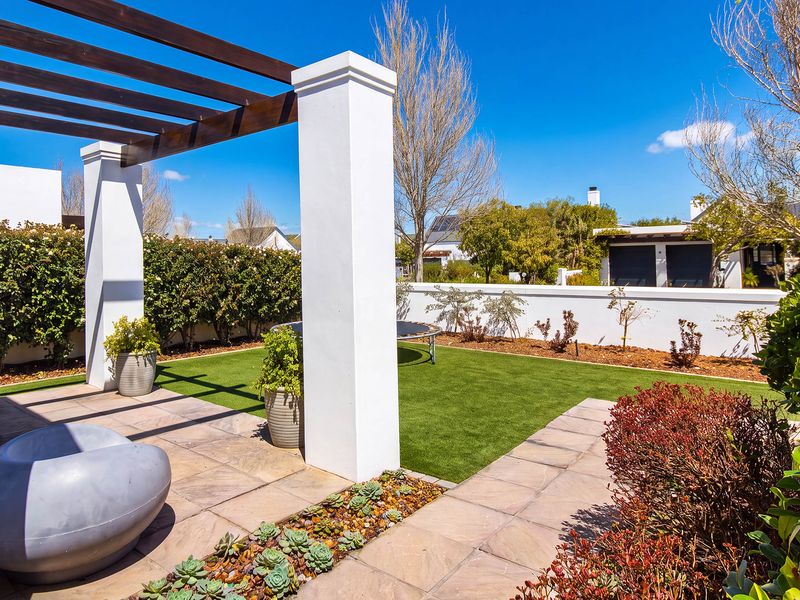 A well-maintained outdoor patio area featuring a timber pergola, paved flooring, and a neat artificial lawn with established boundary walls.