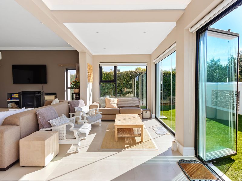 Bright open-plan living area featuring large stacking glass doors that open onto the garden, tiled floors, and a built-in fireplace.