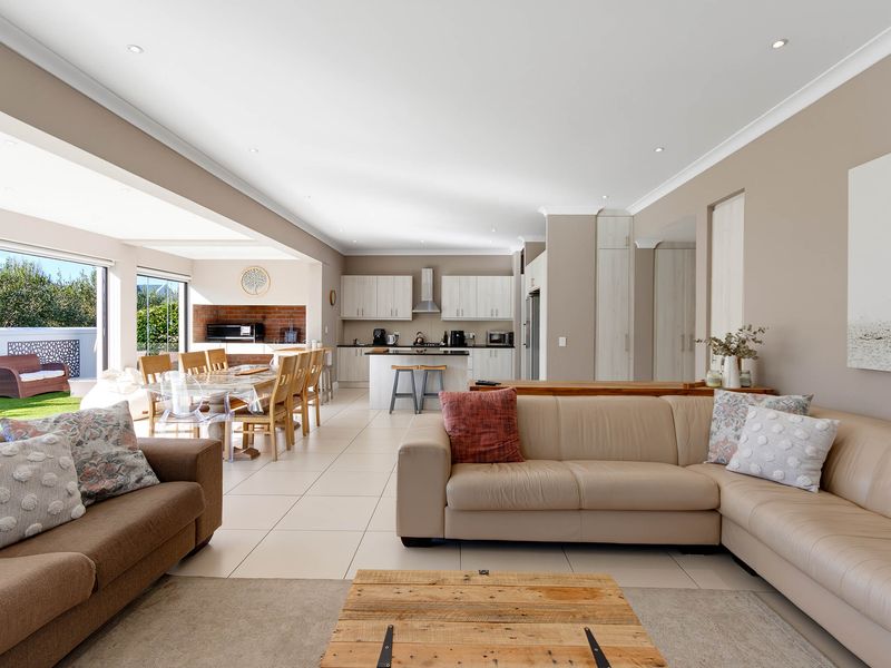 Spacious open-plan living and kitchen area featuring modern cabinetry, tiled floors, and seamless flow to an outdoor patio with a built-in brick braai.
