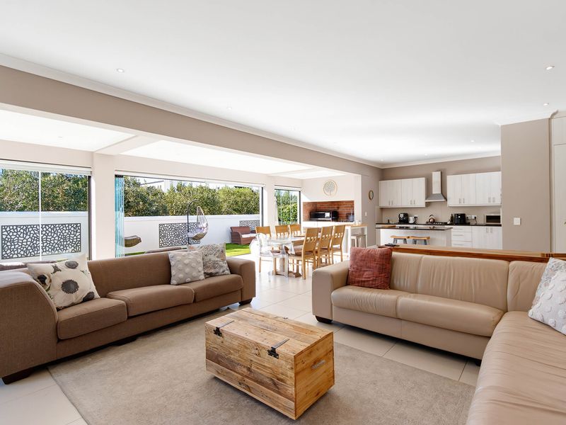 Spacious open-plan living area featuring a modern kitchen with built-in cabinetry, flowing seamlessly through stacking doors to an outdoor patio and garden area.