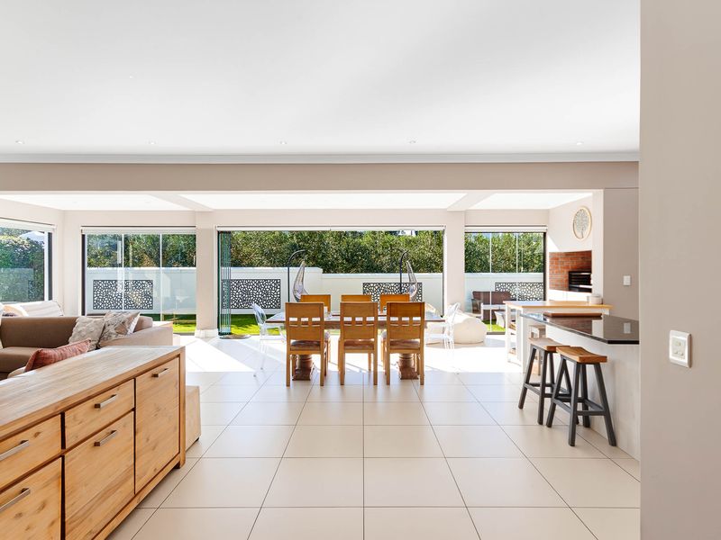 Spacious open-plan living and dining area featuring a built-in braai, kitchen island with granite countertops, and seamless access to the garden through stacking glass doors.