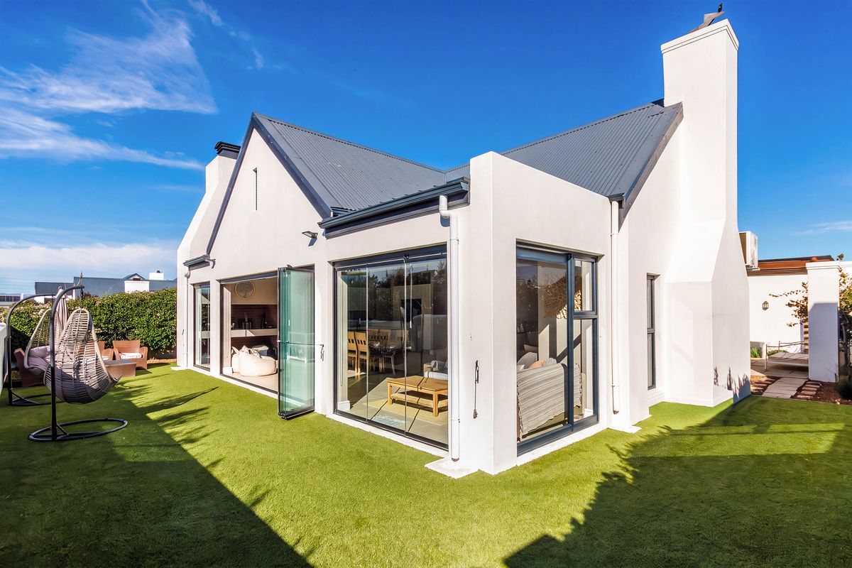 Rear view of a modern home featuring a corrugated metal roof, large bi-fold glass doors, and a well-maintained artificial lawn area.