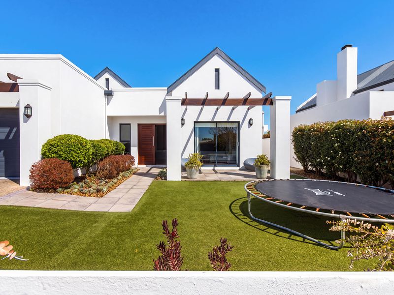 A well-maintained rear exterior featuring a modern white facade, timber pergola, paved patio area, and neatly landscaped artificial lawn.