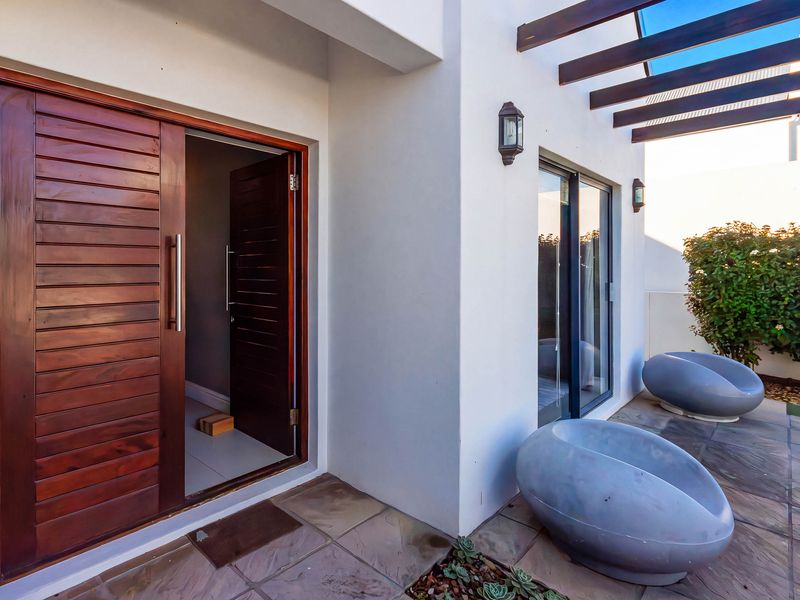 A covered patio area featuring stone tile flooring, a timber pergola, and modern sliding door access to the interior living space.