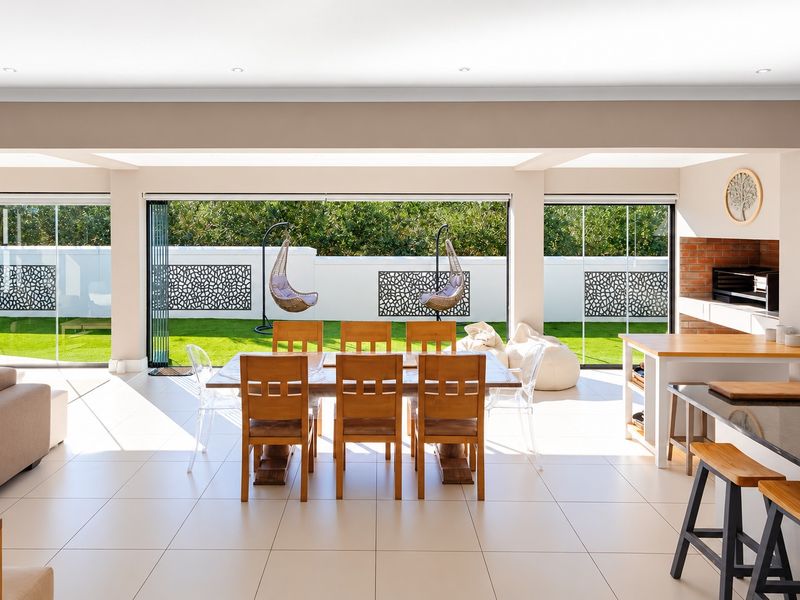 Spacious open-plan living and dining area featuring tiled floors, a built-in braai with brick detailing, and large sliding doors opening to the garden.