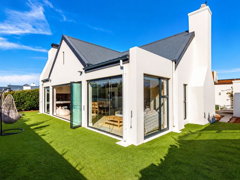 A modern rear exterior view of the house featuring a well-maintained artificial lawn, large glass windows, and bi-fold doors leading to the interior.