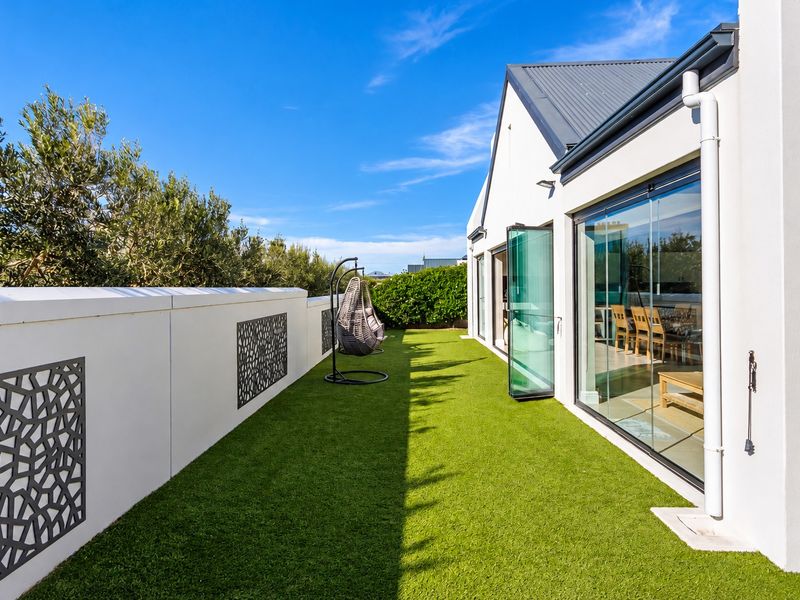 A modern outdoor patio area featuring artificial turf, decorative privacy screens, and seamless bi-fold glass doors connecting to the interior living space.