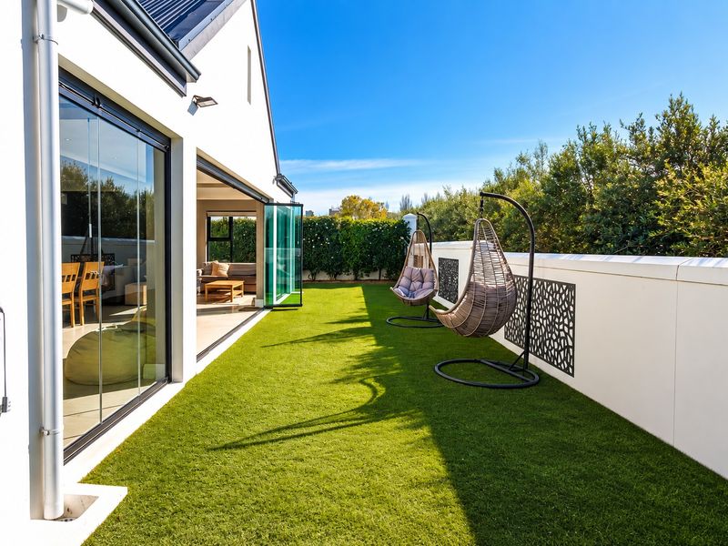A modern outdoor patio area featuring artificial turf, decorative boundary wall panels, and seamless indoor-outdoor flow through large stacking glass doors.