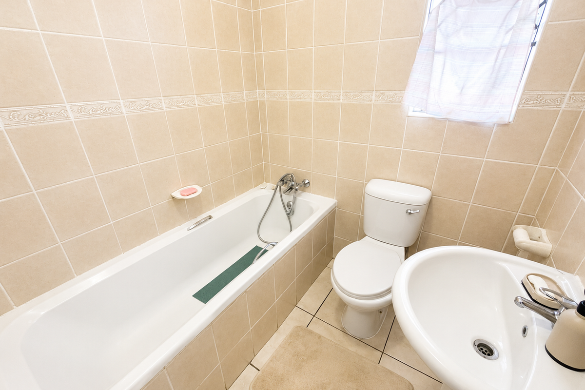 A functional bathroom featuring a bathtub with handheld shower, pedestal basin, and toilet, finished with neutral ceramic wall and floor tiles.
