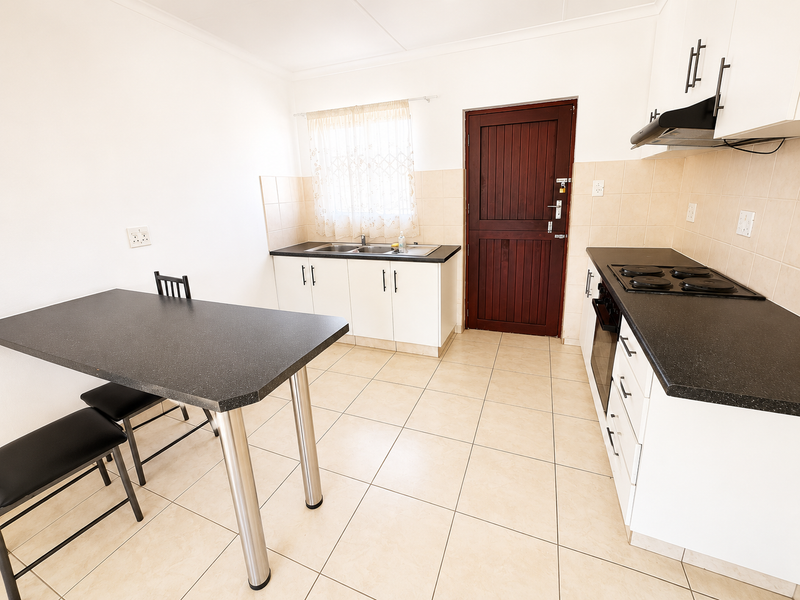 A functional kitchen featuring white cabinetry, dark laminate countertops, built-in oven and hob, tiled splashbacks, and tiled flooring with direct access to an exterior door.