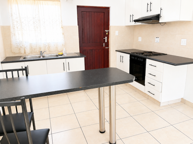 Functional kitchen featuring white cabinetry, dark laminate countertops, built-in oven and hob, tiled splashbacks, and a convenient breakfast bar area.