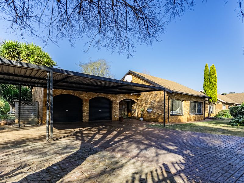 Front view of a brick house featuring a double carport, double garage, and extensive paved driveway area.