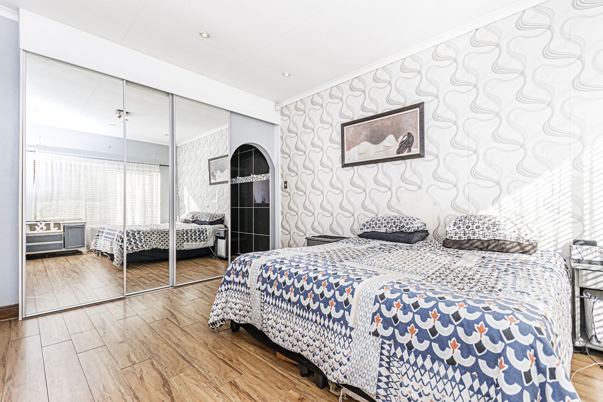 A bedroom featuring laminate flooring, recessed downlights, and large mirrored sliding wardrobe doors, with an arched entrance leading to an en-suite bathroom.