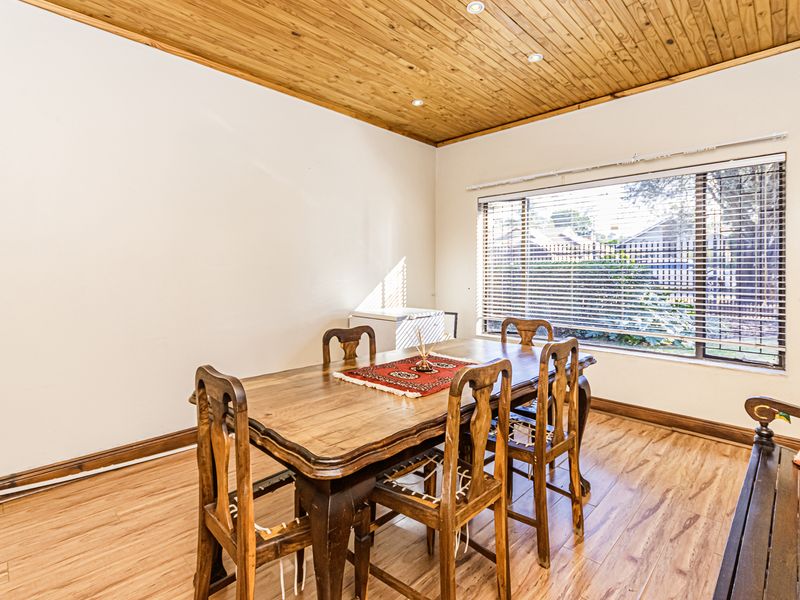 Dining room featuring timber ceiling paneling, laminate flooring, and large window with venetian blinds, providing a warm and functional space.