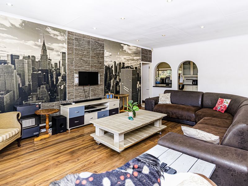 Spacious living room featuring laminate flooring, recessed downlighting, and a stone-clad feature wall with integrated archway access to the adjacent kitchen area.