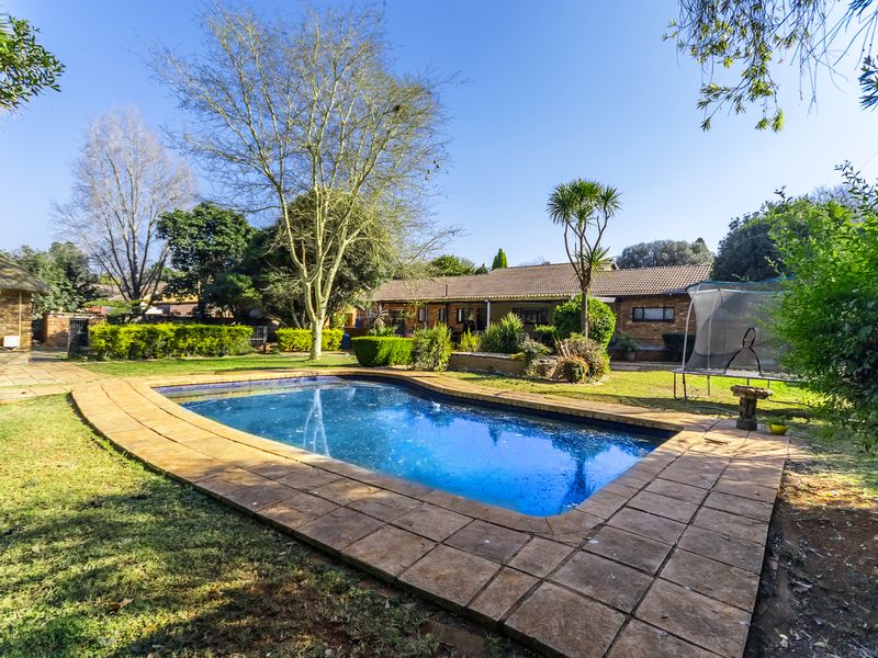 A spacious backyard featuring a swimming pool with a paved surround, set within a well-established garden and brick-built residential property.