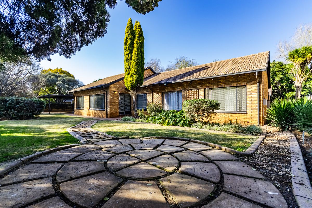 Rear view of a brick house featuring a circular stone patio, landscaped garden, and a stone pathway leading to the residence.