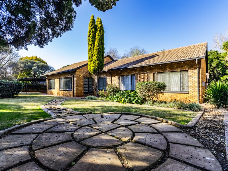 Rear view of a brick house featuring a circular stone patio, landscaped garden, and a stone pathway leading to the residence.