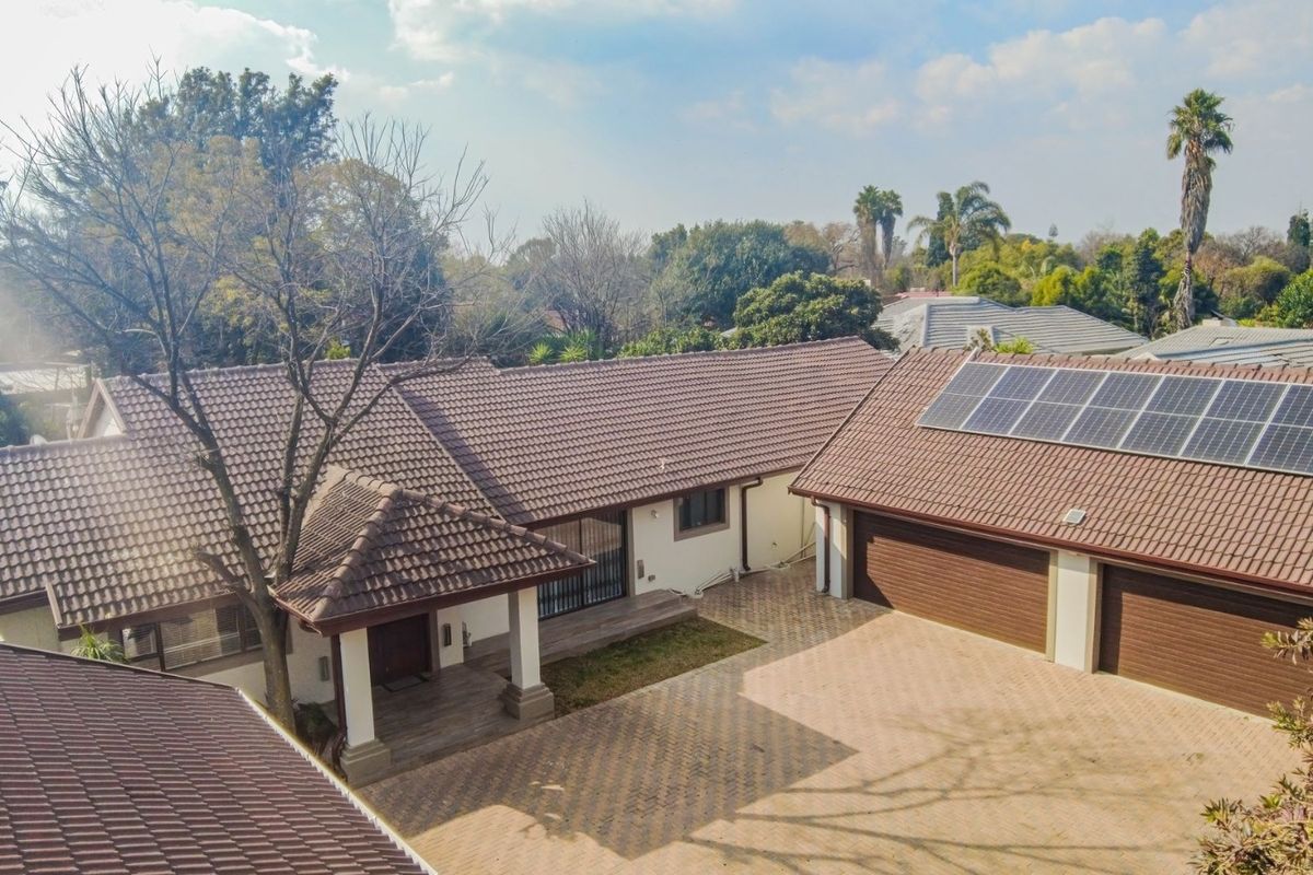 Aerial view of a residential property featuring a tiled roof with solar panels, a paved driveway, and a double garage.