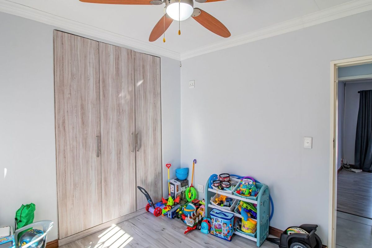A bedroom featuring light wood-look laminate flooring, built-in cupboards with a modern finish, and a ceiling fan.