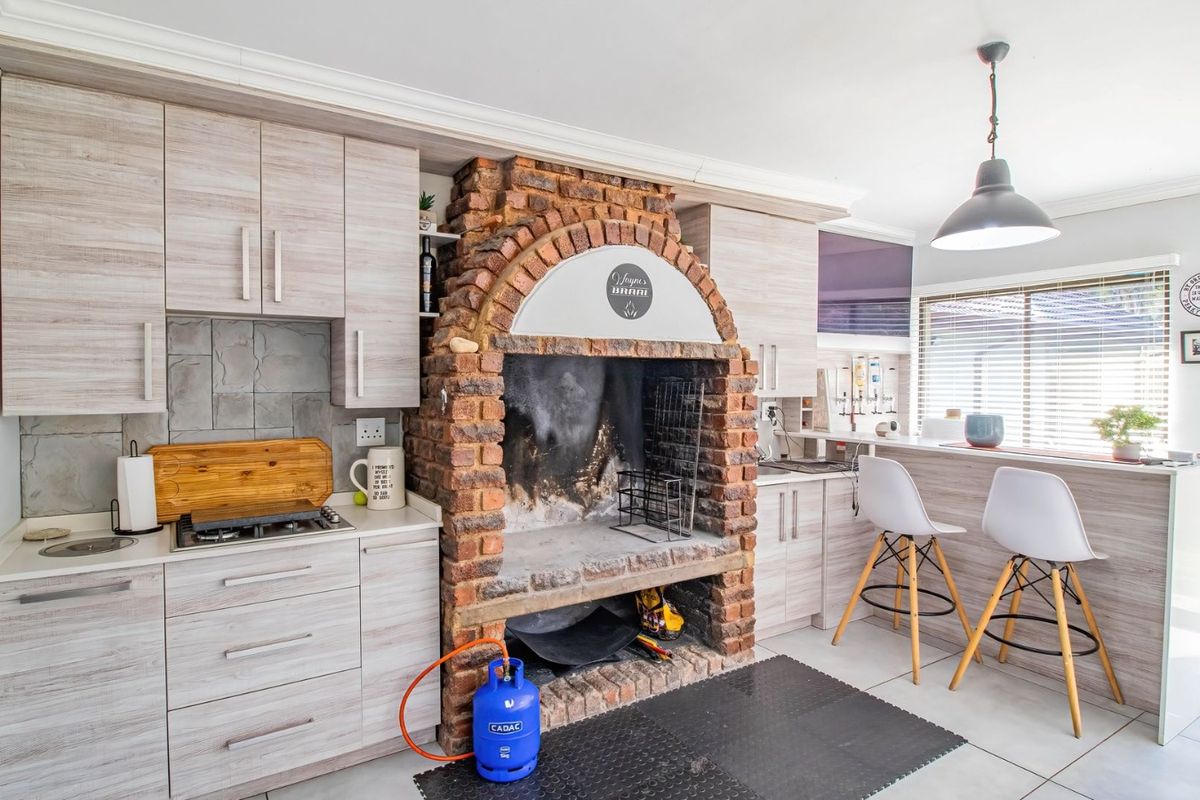 A functional kitchen featuring a prominent built-in brick braai, light wood-grain cabinetry, gas hob, and a breakfast bar area.