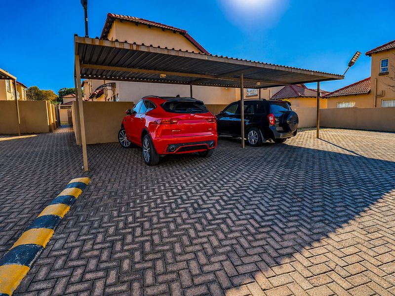 A paved outdoor parking area featuring a covered carport structure within a townhouse complex.