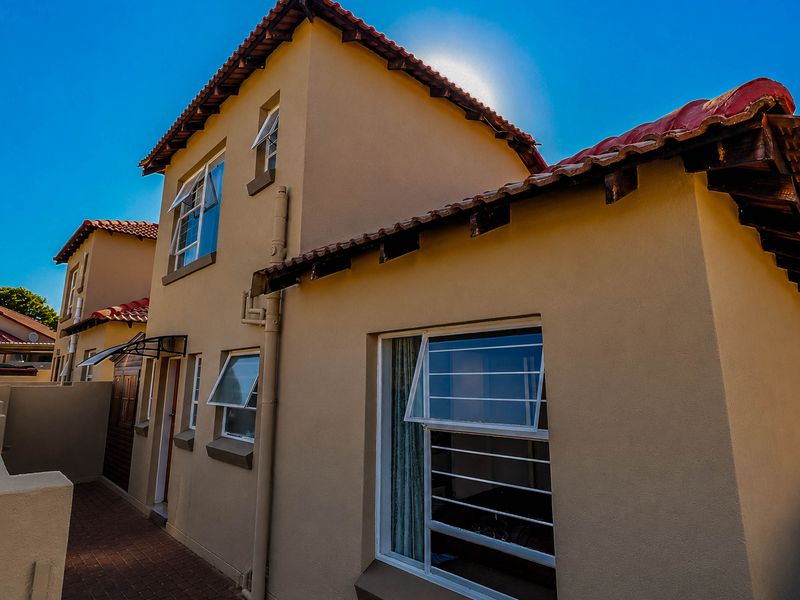 Rear exterior view of a two-story townhouse featuring terracotta roof tiles, stucco walls, and paved walkway access.