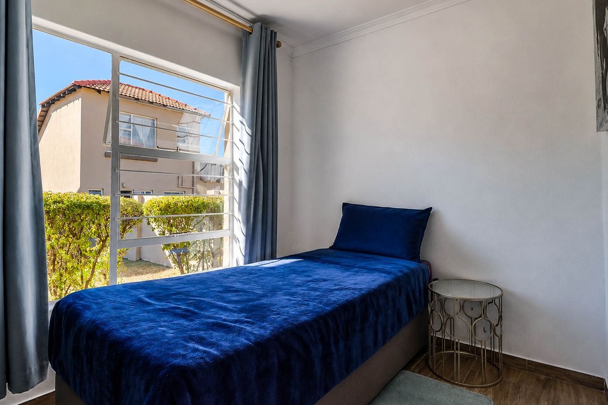 A bright bedroom featuring tiled flooring, neutral walls, and a large window with views of the surrounding townhouse complex.