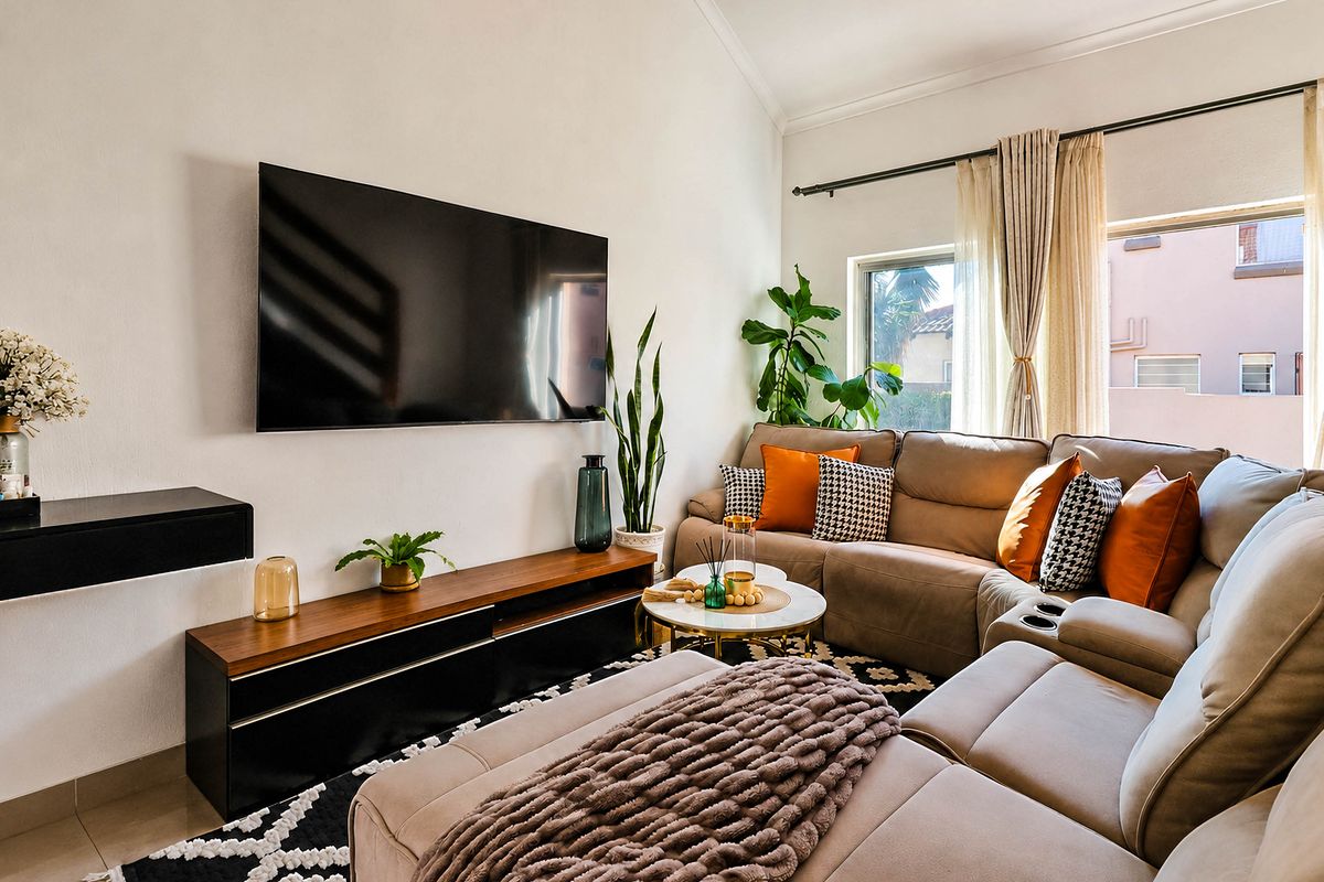 A bright and well-maintained living room featuring a vaulted ceiling, tiled flooring, and large windows with curtain rails.