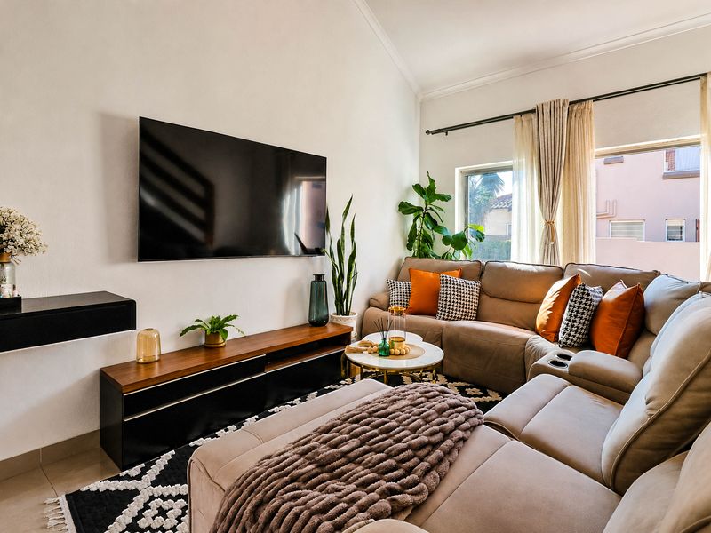 A bright and well-maintained living room featuring a vaulted ceiling, tiled flooring, and large windows with curtain rails.