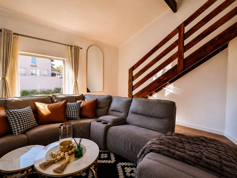 A well-lit living room featuring a wooden staircase railing, exposed ceiling beam, and laminate flooring, creating a warm and inviting atmosphere.