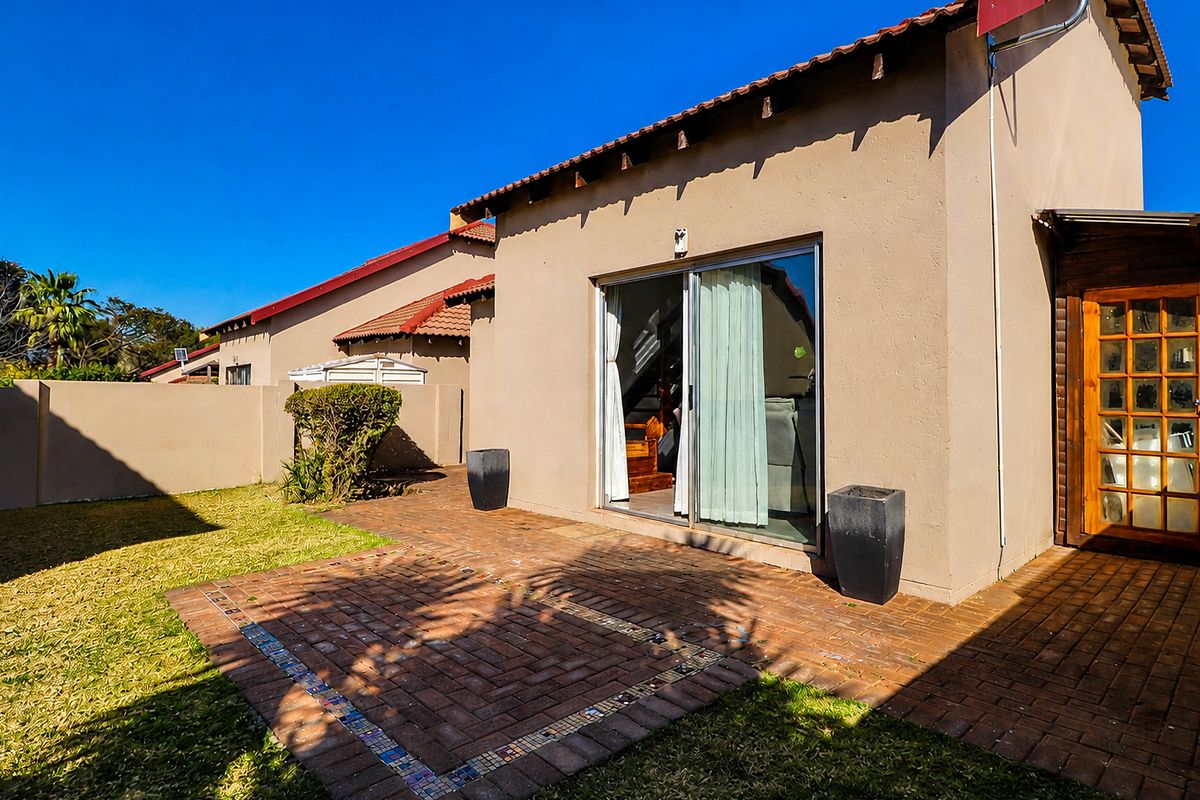 Rear view of the townhouse featuring a brick-paved patio, sliding glass door access, and a private garden area with perimeter walling.