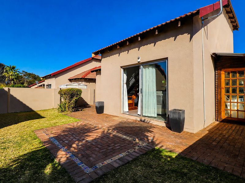Rear view of the townhouse featuring a brick-paved patio, sliding glass door access, and a private garden area with perimeter walling.