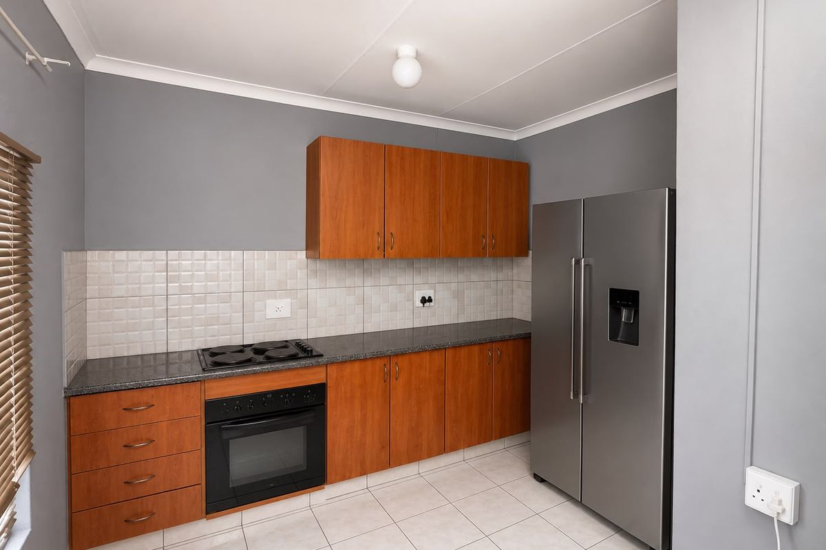 A functional kitchen featuring wood-finish cabinetry, granite countertops, a built-in oven and hob, and neutral tiled flooring.