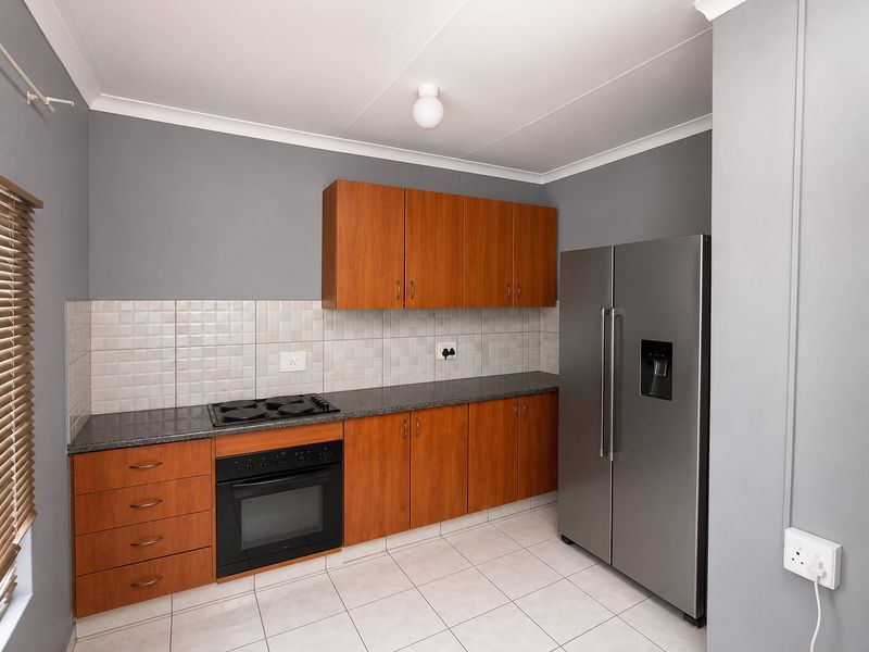 A functional kitchen featuring wood-finish cabinetry, granite countertops, a built-in oven and hob, and neutral tiled flooring.