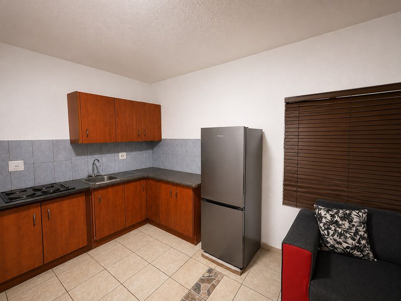 A functional kitchen featuring wood-finish cabinetry, laminate countertops, a built-in hob, and tiled flooring with a neutral backsplash.