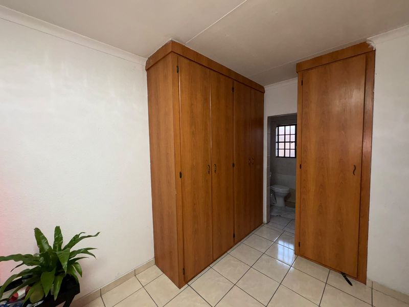 A bedroom featuring built-in wooden cupboards, tiled flooring, and an adjoining en-suite bathroom area.
