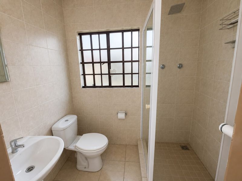 A clean, functional bathroom featuring a walk-in shower with a rain shower head, pedestal basin, and neutral floor-to-ceiling tiling.
