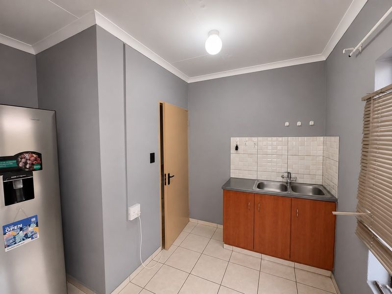 Functional laundry area featuring a double stainless steel sink, laminate cabinetry, tiled splashback, and neutral ceramic floor tiles.
