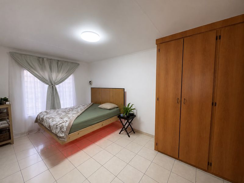 A bedroom featuring tiled flooring, a built-in wooden wardrobe, and a ceiling light fixture.