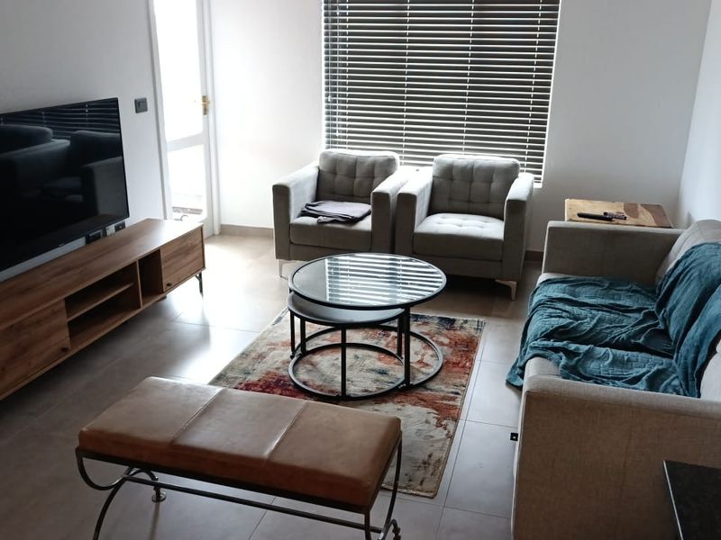 A well-lit living room featuring neutral tiled flooring and venetian blinds, providing a comfortable and functional space.
