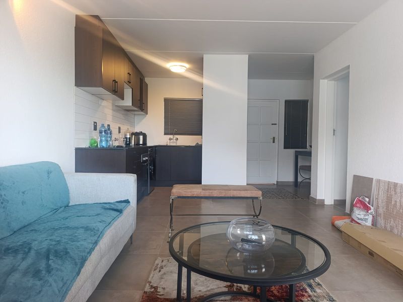 Open-plan living area featuring a modern kitchen with dark cabinetry, tiled flooring, and direct access to the main entrance.