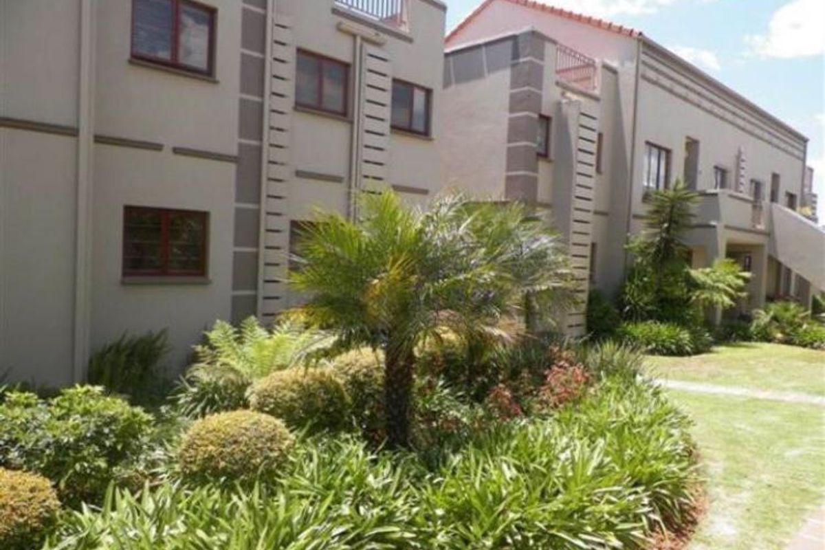 Exterior view of the apartment complex featuring landscaped gardens, paved pathways, and upper-level balconies with modern stucco facade detailing.