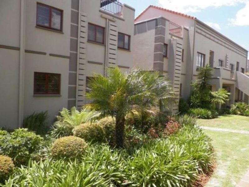 Exterior view of the apartment complex featuring landscaped gardens, paved pathways, and upper-level balconies with modern stucco facade detailing.
